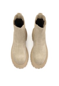 Bottines en daim beige avec un design montante et des semelles en caoutchouc épaisses. Équipées d'une languette à l'arrière et d'une texture lisse.