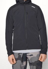 Giubbotto leggero nero con zip completa, cappuccio e tasca sul petto; presenta una texture liscia e il logo POC sulla spalla.