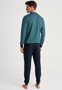 Herenpyjama's met een groen en marineblauw ruitpatroon op de bovenkant met ribgebreide manchetten, gecombineerd met effen marineblauwe broek, gemaakt van een zachte stof.