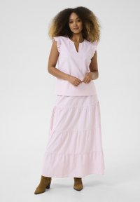 Haut sans manches rayé rose et blanc avec des manches volantées, associé à une jupe longue à volants dans le même motif. Bottes à talons carrés brunes.