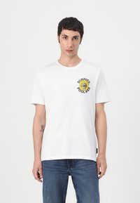 T-shirt en coton blanc avec un col rond et une illustration à l'avant d'un tournesol avec le texte "SUNNIES POOLBAR" en noir au-dessus et en dessous.