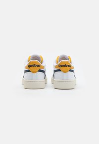 Zapatillas de piel blanca con detalles en amarillo y navy, con cuellos acolchados y suelas texturizadas, con la marca "Reebok" en la parte trasera.