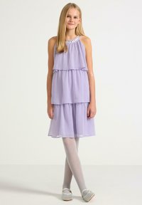 Fialová bezramenní šaty s vrstvenými volány, zdobené korálkovým výstřihem. V kombinaci s lehce šedými punčochami a tkanými nazouvacími botami.