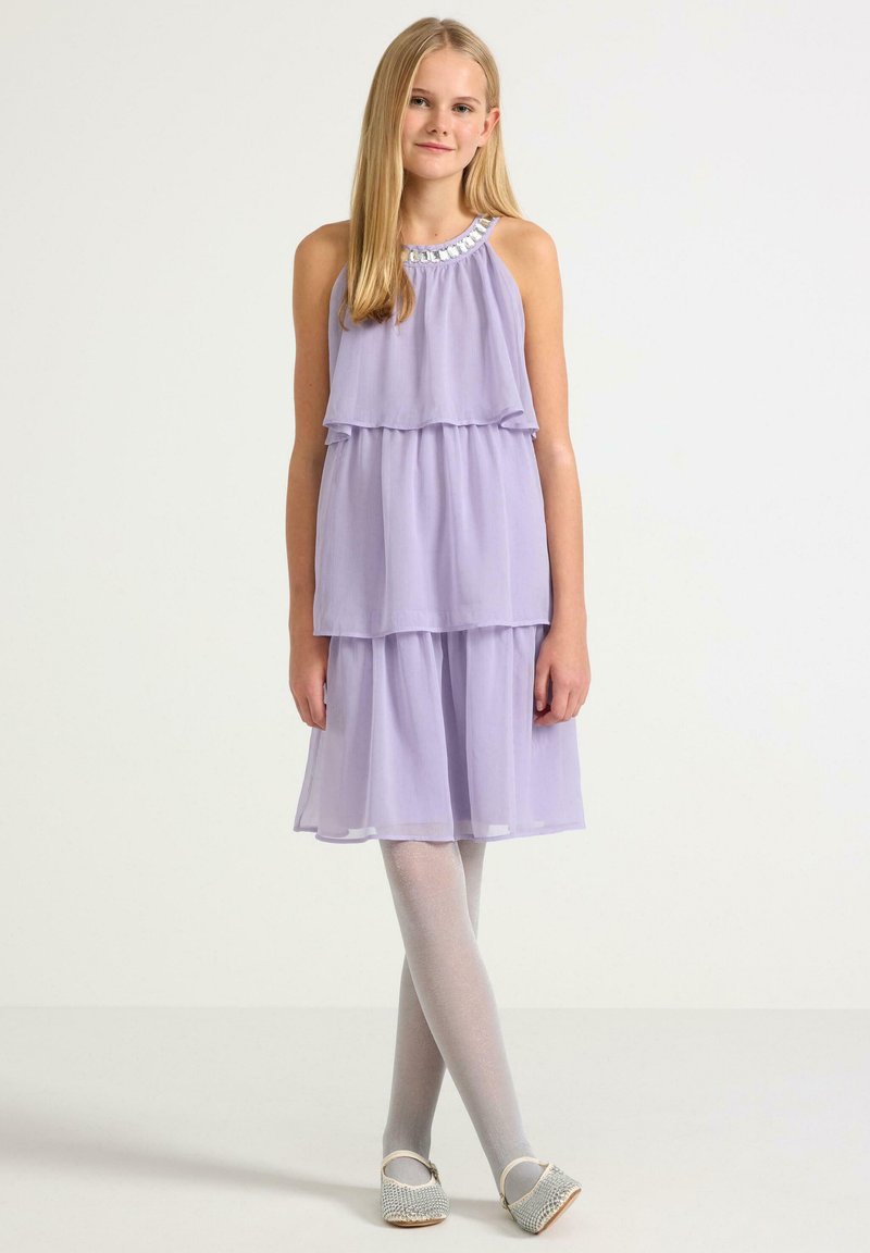 Fialová bezramenní šaty s vrstvenými volány, zdobené korálkovým výstřihem. V kombinaci s lehce šedými punčochami a tkanými nazouvacími botami.