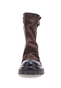 Bota de ante marrón con puntera redondeada negra, de altura hasta el tobillo y un detalle de hebilla en el lateral. Presenta un upper texturizado y una suela de goma gruesa.