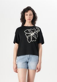 T-shirt en coton noir à manches courtes, avec une grande broderie florale blanche sur le devant. Associé à un short en denim bleu clair.