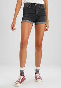 Pantalones cortos de mezclilla de tiro alto en negro con dobladillos enrollados, con remaches de cobre. Combinados con zapatillas rojas y calcetines a rayas.