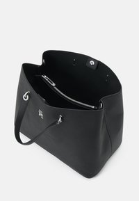 Svart teksturert tote bag med sølvhardware, åpen topp, enkel håndtak og glidelåslomme inni. Har et logoelement på siden.