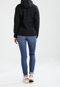 Black hooded jacket with a smooth, matte finish. Paired with light blue denim jeans and white sneakers. Focus on clean lines and contemporary fit.