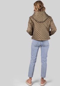 Brun kviltet jakke med hætte, med diamantmønster og elastiske manchetter, parret med lyseblå jeans og beige slip-on sko.