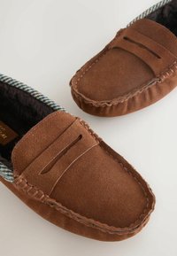 Ruskeat mokkasiinityyppiset loafersit, joissa on lämmin vuori, ruudullinen reunus ja ompeleilla koristeltu päällinen. Tasapohjainen muotoilu.