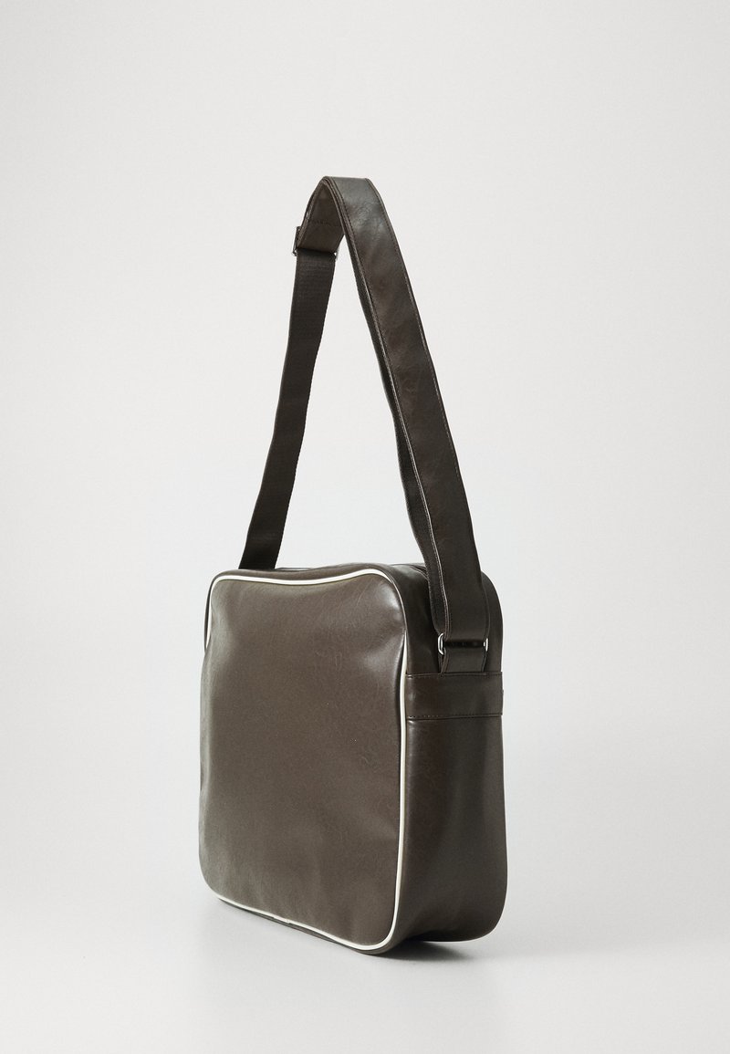 Sac messager en cuir marron avec une texture lisse, doté de passepoils blancs, d'une longue bandoulière réglable et d'une forme rectangulaire avec une fermeture éclair.