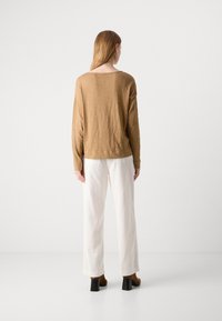 Brun langermet topp med en avslappet passform, kombinert med hvite ribbede vide bukser og brune hælboots. Enkel, teksturert design.