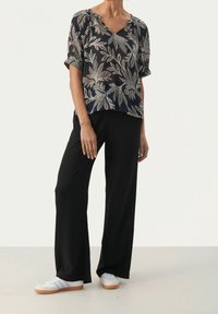 Blusa floreale navy con maniche corte, scollo a V e dettagli dorati abbinata a pantaloni neri a gamba larga e sneakers bianche. Tessuto con una texture liscia.
