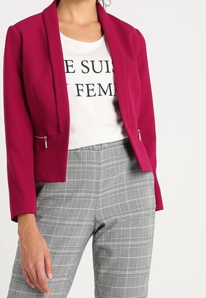 Fuchsiový blazer s klopami, bočními zipovými kapsami, v kombinaci s bílým grafikem tričkem a šedými kostkovanými kalhotami. Textura je hladká.