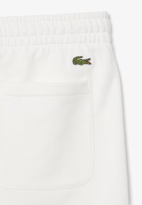 Pantalones cortos de algodón blancos con una cintura elástica, que presentan un pequeño logo de cocodrilo bordado en verde en el bolsillo trasero.