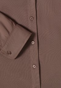 Gros plan d'une chemise marron à manches longues montrant le poignet avec un bouton et la patte de boutonnage avant avec quatre boutons, tissu texturé.