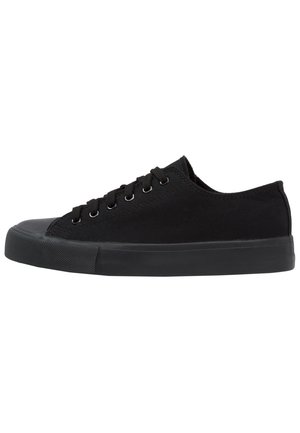 Sneaker nera in tela bassa con suola e punta in gomma nera, con lacci neri inseriti in sei occhielli metallici.