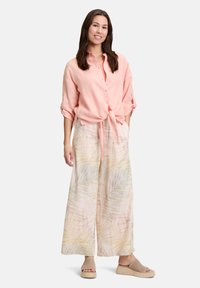 Lys pink linned skjorte med knaplukning, bundet i taljen, parret med brede bukser med et blødt, pastel palmebladsmønster. Neutrale slip-on sko.