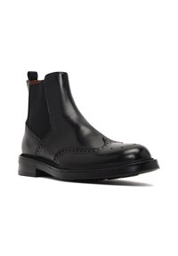 Botín Chelsea negro de cuero con detalles de brogue, paneles laterales elásticos y una resistente suela de goma negra. Textura suave y diseño elegante.