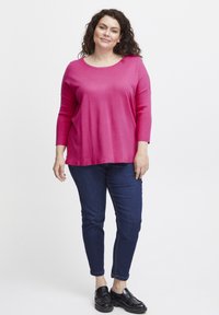 Blusa de manga larga fucsia con cuello redondo, combinada con jeans ajustados de color azul oscuro y mocasines negros. La tela parece suave y texturizada.