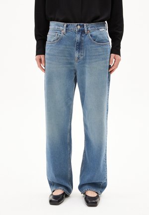 Jeans in denim chiaro con design a gamba larga, vita alta, tasche anteriori e una leggera texture sbiadita; abbinati a ballerine nere.