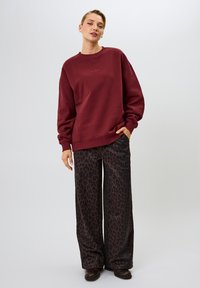 Bordeaux sweatshirt met een ontspannen pasvorm, lange mouwen en een ronde hals, gecombineerd met zwarte wijde broek met een luipaardprint.