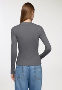 Szary, długi rękaw bluzka z ryżowego materiału, z okrągłym dekoltem, zestawiona z niebieskimi dżinsami o wysokim stanie.