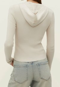 Rippiger, hellbeiger Hoodie mit einem Rückenausschnitt und langen Ärmeln, kombiniert mit hochtaillierten, hellblauen Jeans mit hinteren Taschen.