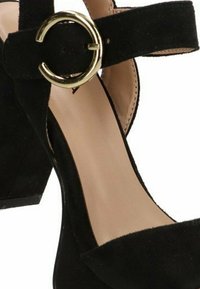 Zapato de tacón alto de ante negro con un tacón ancho, una correa en el tobillo con un hebilla circular dorada y un diseño de punta afilada.