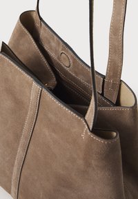 Tan suède schoudertas met een zachte textuur, voorzien van een gestikte rand, een ritssluiting binnenvak en lange schouderbanden.