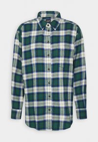 Chemise à manches longues boutonnée avec motif à carreaux vert, blanc et bleu, col pointu et poche poitrine à l’avant.