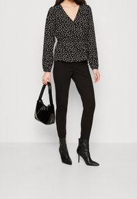 Czarna kwiecista bluzka wiązana z długimi rękawami, zestawiona z czarnymi dopasowanymi spodniami i błyszczącą czarną torebką, uzupełniona czarnymi, szpiczastymi botkami za kostkę.