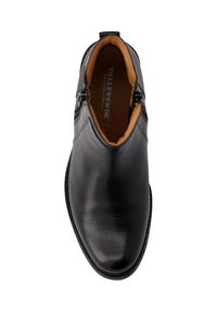 Stivali alla caviglia in pelle nera con finitura liscia, dotati di cerniere laterali e una fodera interna color cammello. Il design è elegante e angolare.