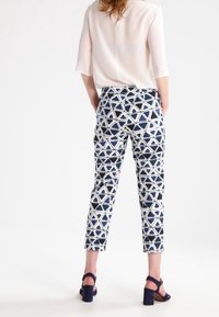 Mönstrade byxor i flera färger i marinblått och vitt med geometriska former, ihopparade med en lätt, halvtransparent blus och klacksandaler.