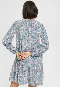 Blommig klänning med lång ärm, rynkad halsringning och flerlagad nederkant. Tillverkad av lättviktigt material med flerfärgade mönster i blått och rosa.