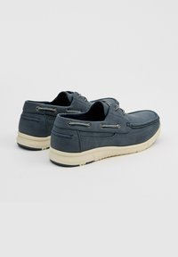 Zapatos de barco de cuero azul marino con suelas blancas; presenta ojales y cordones plateados; punta redondeada y diseño acolchado para mayor comodidad.