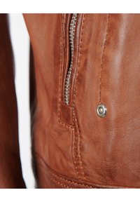 Gros plan sur une veste en cuir marron, avec une fermeture éclair argentée, des détails cousus et un accent en bouton-pression. Texture lisse avec une finition naturelle.