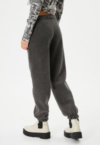 Grijze, zachte joggingbroek met een relaxte pasvorm, gegolfde enkels en een elastische tailleband, gecombineerd met beige robuuste laarzen.