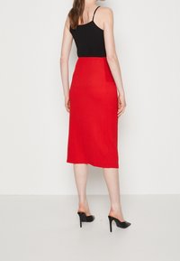 Jupe midi rouge côtelée associée à un débardeur noir ajusté et des chaussures à talons hauts noires. Texture lisse, silhouette près du corps.