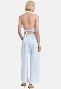 Dvodijelni outfit sastavljen od halter crop topa i širokih hlača. Prugasti uzorak u svijetloplavoj i bijeloj boji, s vezanjem na leđima.