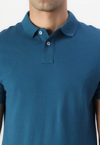 Tyrkisk polo skjorte laget av teksturert stoff har klassisk krage, to knapper på fronten og korte ermer.
