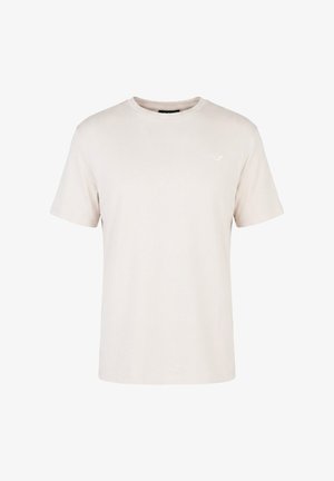 T-shirt beige clair uni à manches courtes et col rond avec un petit logo blanc sur le côté gauche de la poitrine.