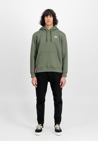Olivově zelená mikina s kapucí a přední kapsou, spárovaná s černými cargo kalhotami s bočními kapsami a zúženým střihem.