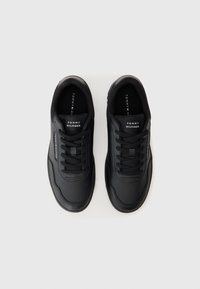 Paire de baskets en cuir noir Tommy Hilfiger avec lacets noirs, vues de dessus sur un fond clair uni.