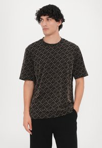 Tricou negru cu mânecă scurtă, prezentând un model geometric în tonuri de bej și culori estompate. Material moale, cu o croială lejeră și decolteu tip crew.