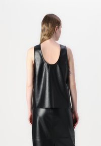 Black sleeveless top made of glossy leather, featuring a rounded back neckline and a loose fit, paired with a matching leather skirt.