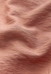 Weicher, zerknitterter rosa Stoff mit subtiler Textur und sanften Falten, die eine fließende, unebene Oberfläche erzeugen.