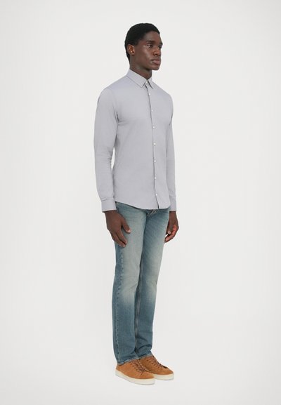 Grå skjorte med lange ermer, paret med lyseblå jeans og brune sneakers. Skjorten har spiss krage og subtilt teksturert stoff.