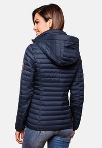 Navy puffer jacket with a hood, featuring quilted design, side pockets, and a small patch accent on the sleeve. Smooth texture.